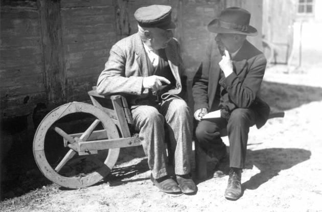 Older men in conversation sitting on old wheelbarrow